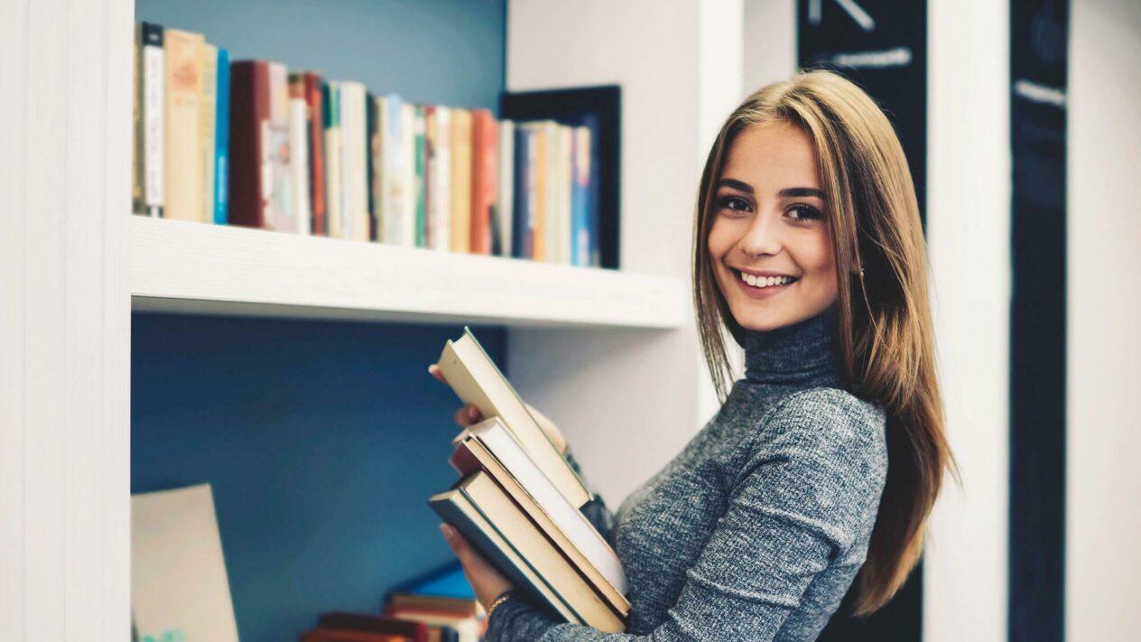Junge Frau mit Büchern im Arm vor einem Bücherregal